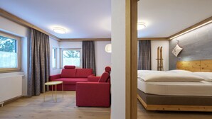 Een kamer met een bed, een rode bank, een klein tafeltje en een raam met gordijnen.