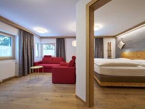 Una habitación de hotel con una cama, un sofá rojo, una mesita y una ventana con cortinas.