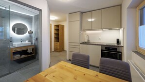 Een moderne keuken met inbouwapparatuur, een houten eettafel en een douchecabine van glas.