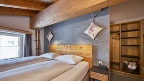 Ein Schlafzimmer mit einem Holz-Kopfteil, einem Bett mit weißer Bettwäsche, einem Nachttisch, einem Holzschrank und einem Fenster mit Vorhängen.