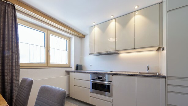 Eine moderne Küche mit Einbauofen, Spüle und einem Fenster mit Vorhängen.