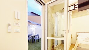 Una stanza con una porta finestra che dà su uno spazio esterno, un letto e un tavolino con sedie.