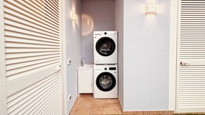 Una lavanderia con due lavatrici affiancate, un piccolo lavandino e una porta con maniglia.