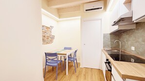 Una cucina compatta con un tavolo di legno, due sedie, una parete decorata in pietra, una porta bianca e un lavandino moderno.