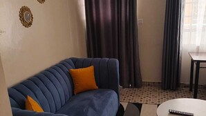 Ein Zimmer mit einem blauen Sofa, einem kleinen runden Tisch und einem Fenster mit Vorhängen.