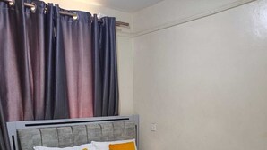 Ein Bett mit grauem Kopfteil, weißer Bettwäsche und zwei orangen Kissen.