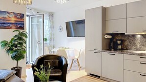 A modern living room with a glass coffee table, a black leather sofa, a dining area with a white table and chairs, and a kitchen with white cabinets and a stone backsplash. - Mine Hygge by Interhome (Koserow)