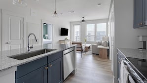 A modern kitchen with a built-in sink, a dining area with a table and chairs, and a living space with a sofa and a TV. - Landing | Modern 2BD, Clubhouse, Gym (San Antonio)