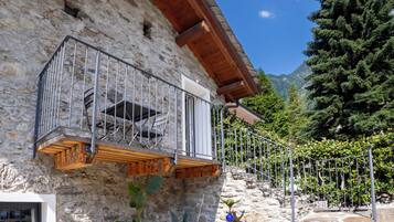 Ein Steinhaus mit Balkon, einer Holzterrasse und einer Bergkulisse.