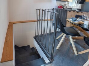 A modern kitchen with a dining area, a staircase with a wooden handrail, and a metal railing. - Cà Coda Rossa by Interhome (Chiavenna)
