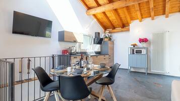 Eine moderne Küche mit Essbereich, Holzbalkendecke, einem an der Wand montierten Fernseher und Blick ins Freie.