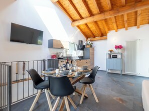 A modern kitchen with a dining area, wooden ceiling beams, a TV mounted on the wall, and a view of the outdoors. - Cà Coda Rossa by Interhome (Chiavenna)