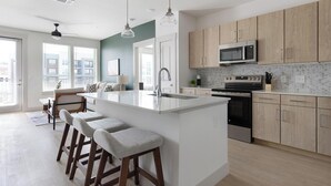 A modern kitchen with a central island, bar stools, wooden cabinets, a microwave, and an oven. - Landing | Beautiful 2BD, Clubhouse, Gym (San Antonio)