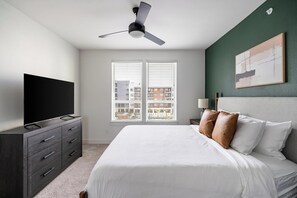 A bedroom with a bed, a TV on a dresser, a ceiling fan, and a window with blinds. - Landing | Stunning 2BD, Clubhouse, Gym (San Antonio)