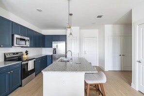 A modern kitchen with dark blue cabinets, stainless steel appliances, and a granite countertop. - Landing | Stunning 2BD, Clubhouse, Gym (San Antonio)