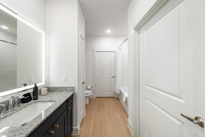 Ein enger Flur mit einem Badezimmer auf der rechten Seite, das eine Toilette, eine Dusche und eine weiße Tür zeigt.