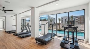Ein Fitnessraum mit Laufbändern, einem Rudergerät und Blick auf einen Pool.