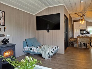 A cozy room with a fireplace, a television mounted on the wall, and a dining area with a table and chairs. - Hellebu by Interhome (Eikerapen)