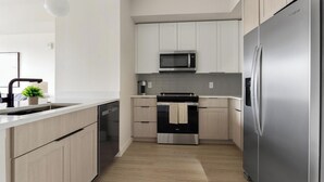Una cocina moderna con electrodomésticos de acero inoxidable, armarios de madera clara y encimera blanca.