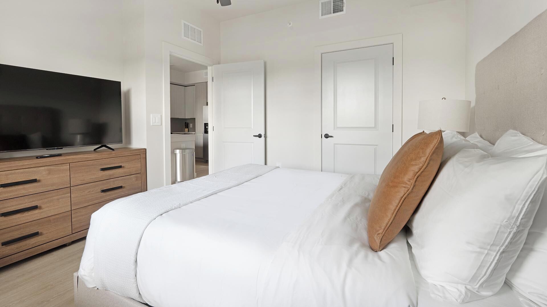 A bedroom with a bed, a TV, a dresser, and a door leading to a bathroom.