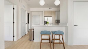 Une cuisine moderne avec des meubles blancs, un évier en acier inoxydable et deux tabourets de bar.