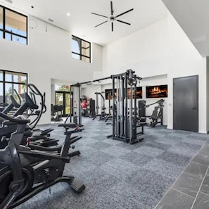A spacious gym with various exercise equipment, large windows, and a high ceiling fan. - Landing | Spectacular 1BD, Gym, Clubhouse (North Fort Myers)