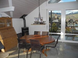 Ein Essbereich mit rundem Tisch und Stühlen, einem Holzschrank und Blick auf eine Stadt durch große Fenster.