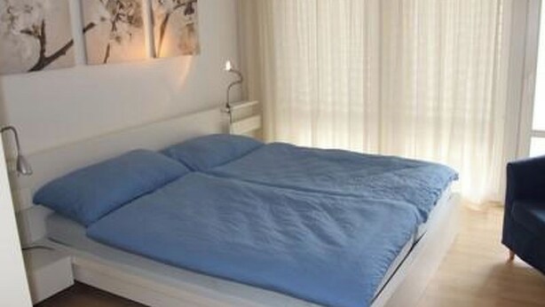 A bedroom with a bed, a nightstand, and a wall-mounted lamp. - Ferienwohnung Gassmann Appartement/Fewo 4-Bett Wohnung mit Dusche, Bad u. Balkon by Interhome (Spiez)