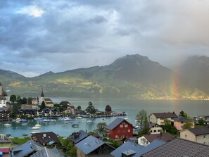 Une ville au bord d’un lac, avec des bâtiments, des bateaux et des montagnes en arrière-plan.