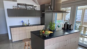 A modern kitchen with a central island, wooden cabinets, and a window with a view of greenery. - Ferienwohnung Gassmann Appartement/Fewo 4-Bett Wohnung mit Dusche, Bad u. Balkon by Interhome (Spiez)