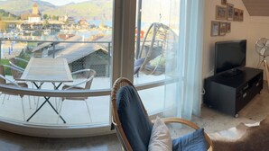 A balcony with a table and chairs, a hanging chair, a television, and framed pictures on the wall. - Ferienwohnung Gassmann Appartement/Fewo 4-Bett Wohnung mit Dusche, Bad u. Balkon by Interhome (Spiez)