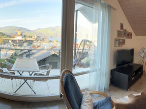 Ein Balkon mit Tisch und Stühlen, einem Hängesessel, einem Fernseher und gerahmten Bildern an der Wand.