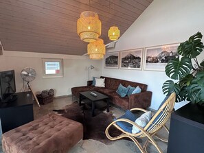 A cozy living room with a brown sofa, a coffee table, a wicker chair, and a large plant. - Ferienwohnung Gassmann Appartement/Fewo 4-Bett Wohnung mit Dusche, Bad u. Balkon by Interhome (Spiez)