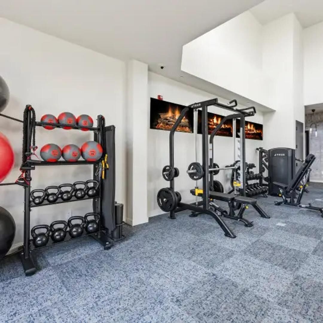 Uma academia com equipamentos de ginástica, um suporte de agachamento fixado na parede e uma lareira.