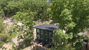 Een modern, verhoogd houten terras met glazen omheining, omringd door dichte bomen.