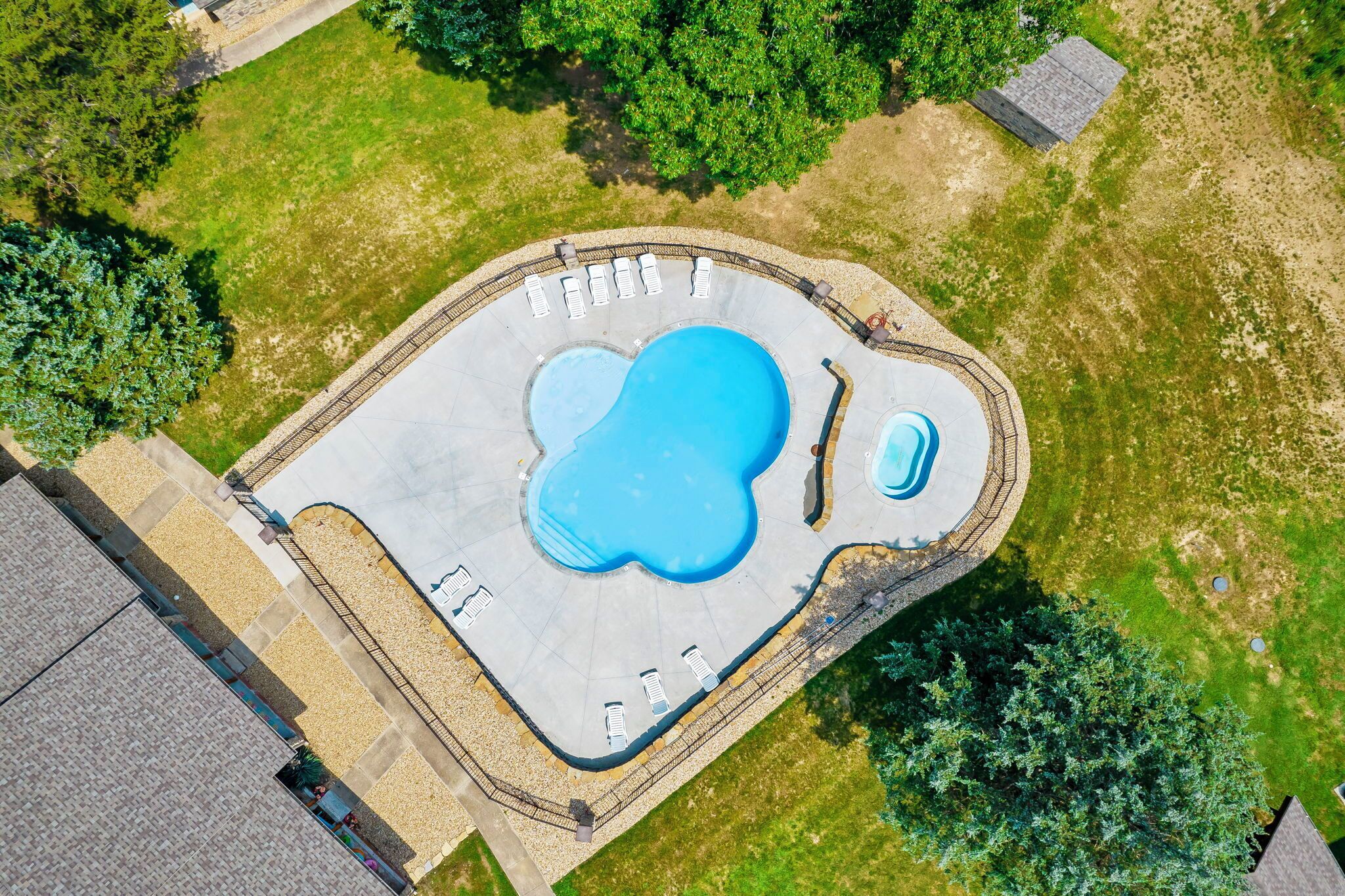 An aerial view of a swimming pool with a unique shape, surrounded by a paved deck and a few lounge chairs.