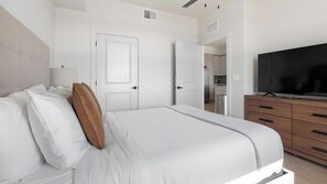 Een slaapkamer met een bed, een televisie, een kapstok en een deur naar een badkamer.