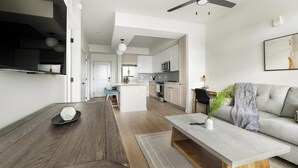 Cocina moderna con armarios blancos, una isla central y un comedor con sofá gris y una mesa de centro.