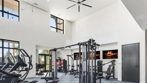 Une salle de sport spacieuse, dotée de divers appareils d’exercice, de grandes fenêtres et d’un ventilateur au plafond.