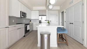 A modern kitchen with white cabinetry, stainless steel appliances, a central island, and a trash can. - Landing | Stunning 1BD, Gym, Clubhouse (North Fort Myers)