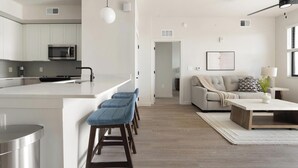 Een moderne keuken met een centraal eiland, barkrukken, een eethoek met een bank en salontafel, en een woonkamer met een sofa en bijzettafeltje.