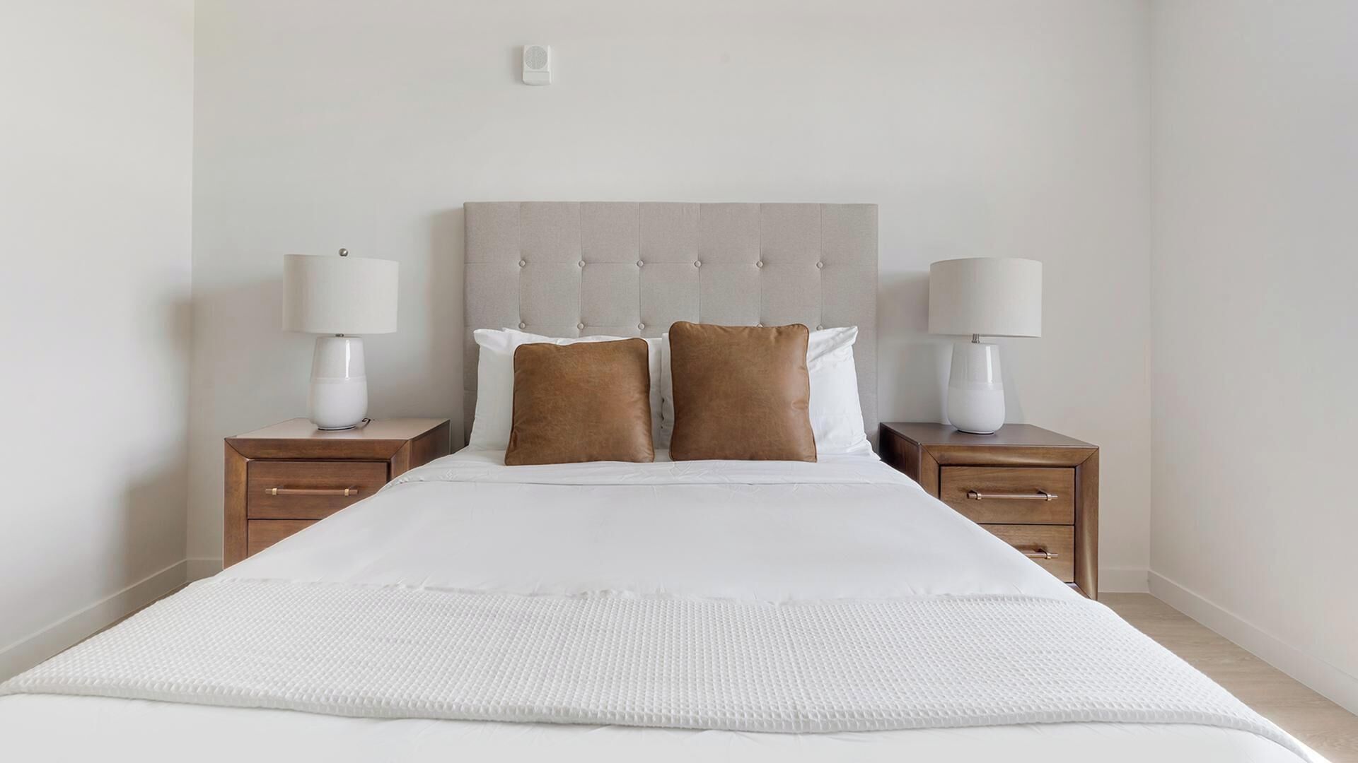 Un lit bien fait, avec une couette blanche, deux oreillers marron et deux tables de chevet dotées de lampes.