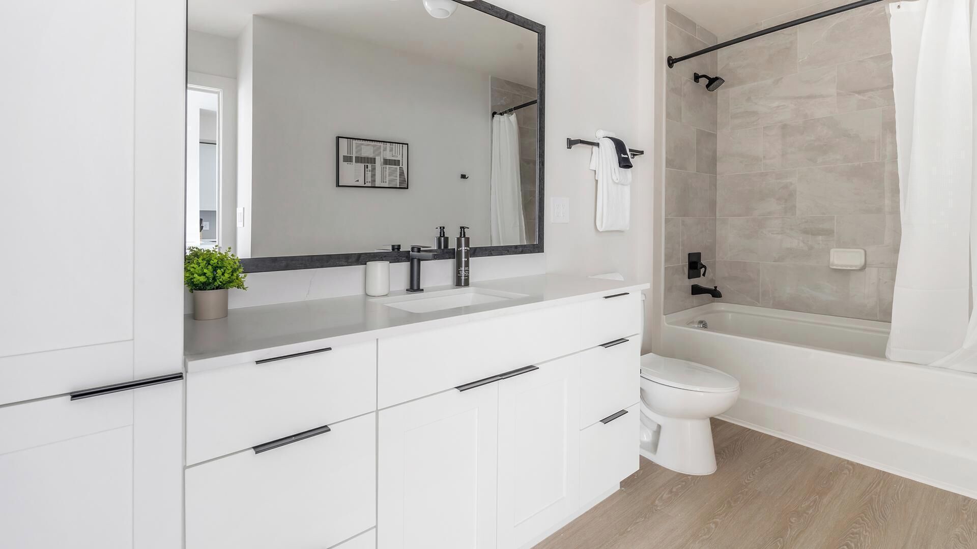 A modern bathroom with a large mirror, white cabinetry, a bathtub, and a toilet.