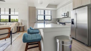 Een moderne keuken met een centraal eiland, roestvrijstalen apparatuur en uitzicht op groen.