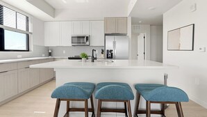 Een moderne keuken met witte kasten, een groot eiland met barstoelen en roestvrijstalen apparatuur.