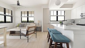 Een moderne keuken met een centraal eiland, een zithoek met een bank en stoelen, en grote ramen met zonwering.