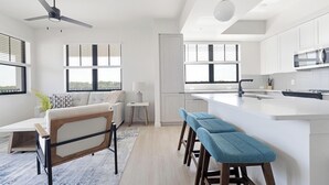 Cocina moderna con una isla central, taburetes de bar, un ventilador de techo y ventanas amplias.