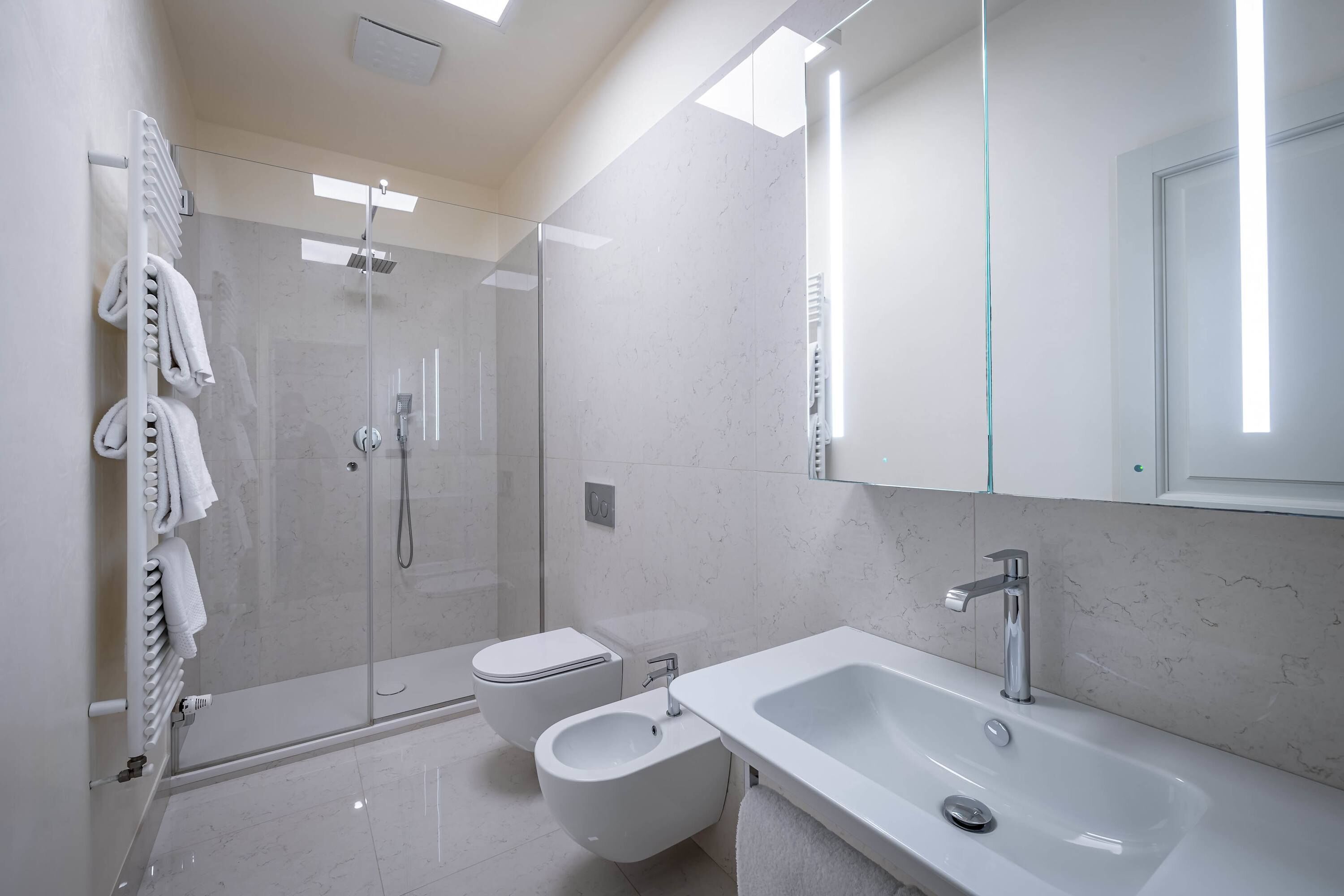 A modern bathroom with a glass-enclosed shower, a bidet, a toilet, and a large sink.
