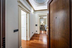 A hallway with wooden flooring, a white door with a black handle, and a ceiling with a decorative design. - Frescoed apartment in the heart of Florence (Firenze)