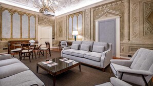 Ein geräumiges Wohnzimmer mit einer Chandelieber, einer Couch, Sesseln und einem Essbereich mit Stühlen und einem Tisch.